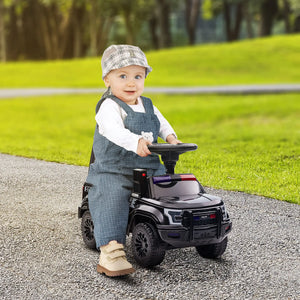 Child sitting on a toy car outdoors with green grass and trees in the background