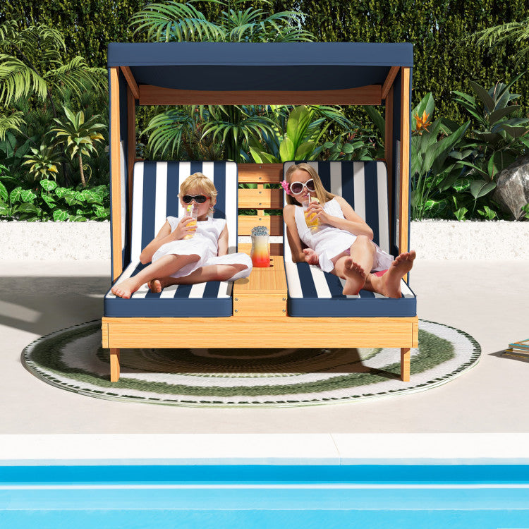 Two children sitting on a striped lounge chair by a pool with a tropical background.