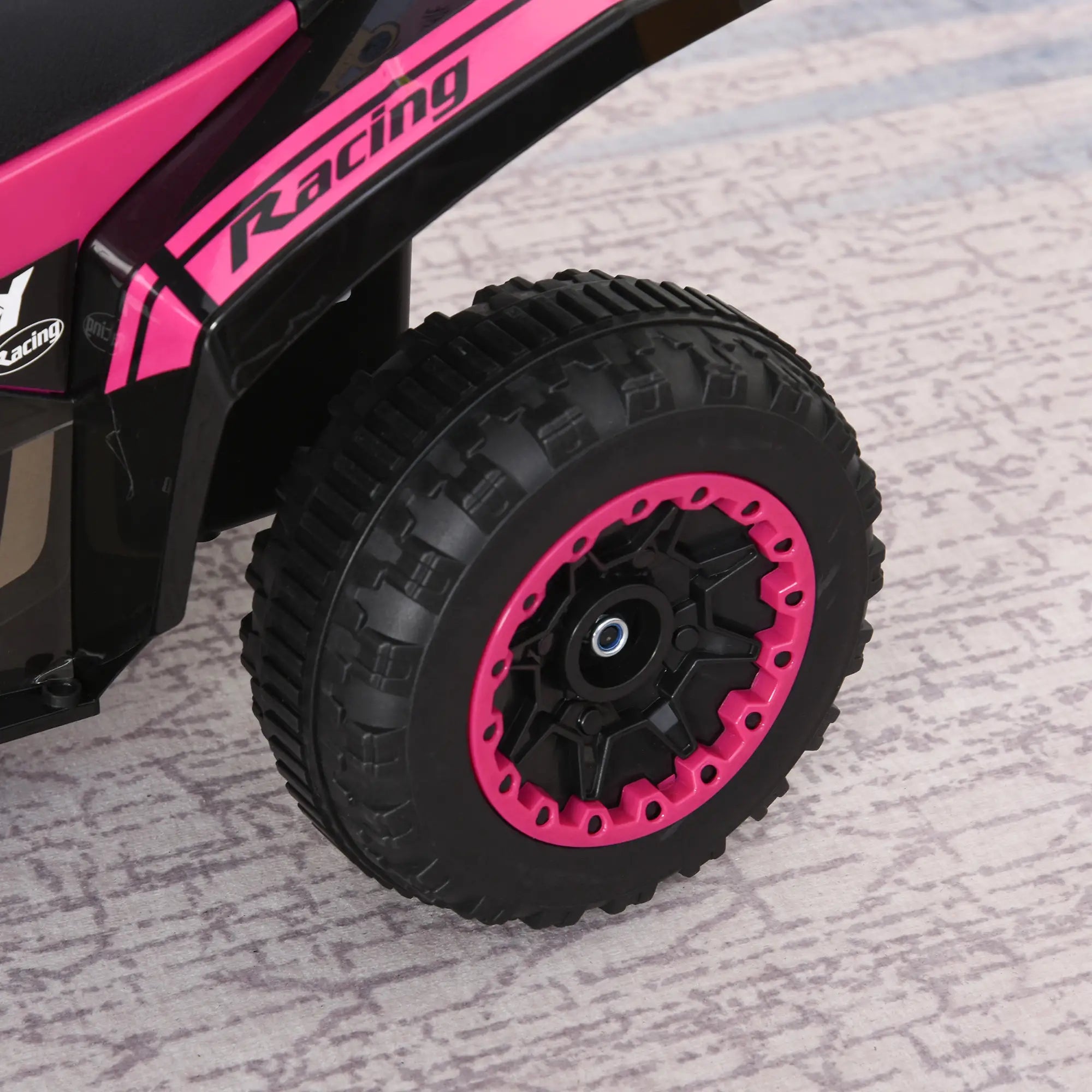 Close-up of a pink and black toy car wheel on a textured surface