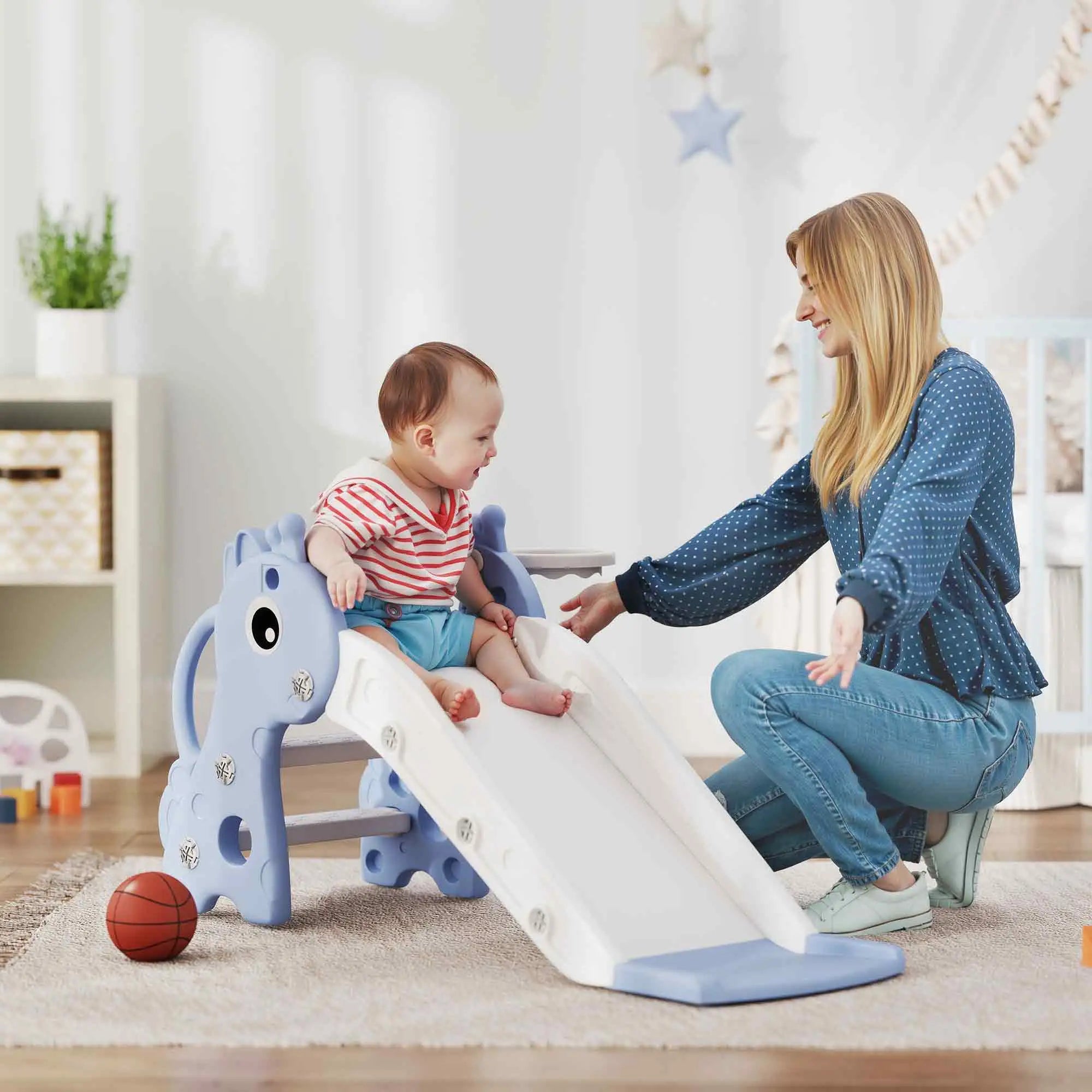 Baby playing on a blue and white slide with a woman in a home setting.