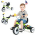Child riding a green tricycle with additional tricycles and a flag in the background