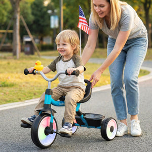 Child riding a tricycle with a woman assisting, in an outdoor setting.