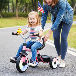 Child on a tricycle with a woman pushing them, both outdoors.