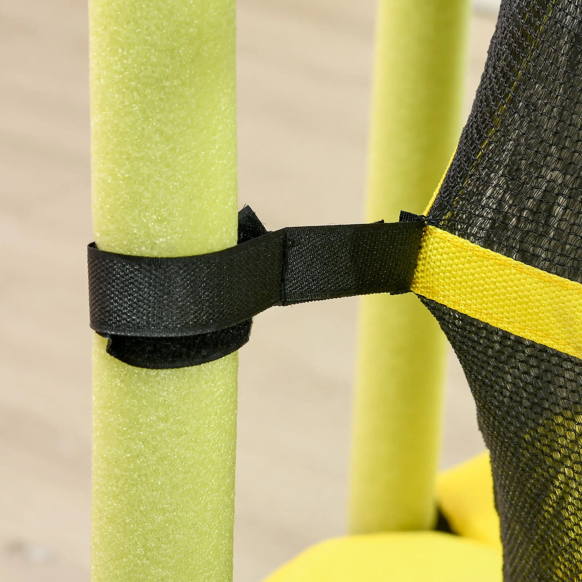 Close-up of a black strap securing green and yellow pool noodles against a neutral background