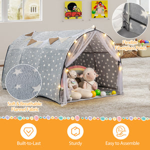 Children's play tent with star pattern, plush toys, and fairy lights on a wooden floor.