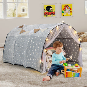Child playing inside a star-patterned play tent with toys on a wooden floor.